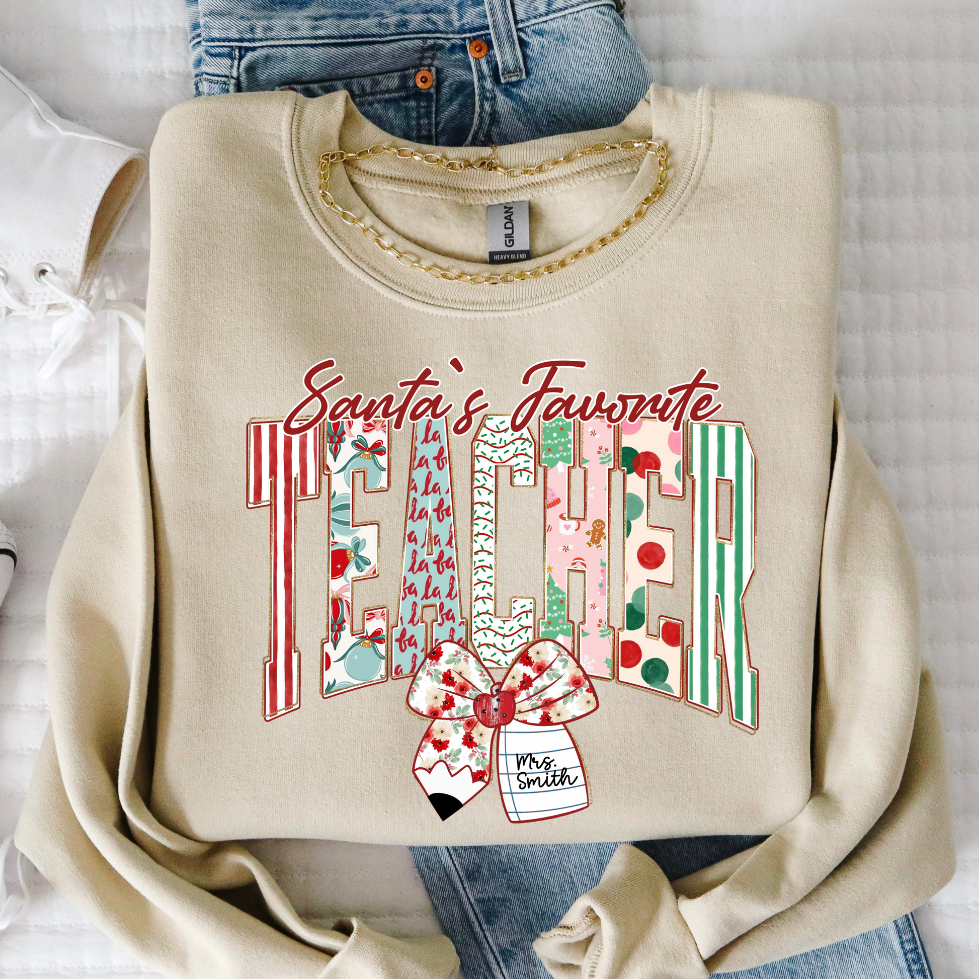 Sand color Santa’s Favorite Teacher Christmas sweatshirt with festive striped letters and bow, displayed in flat lay.
