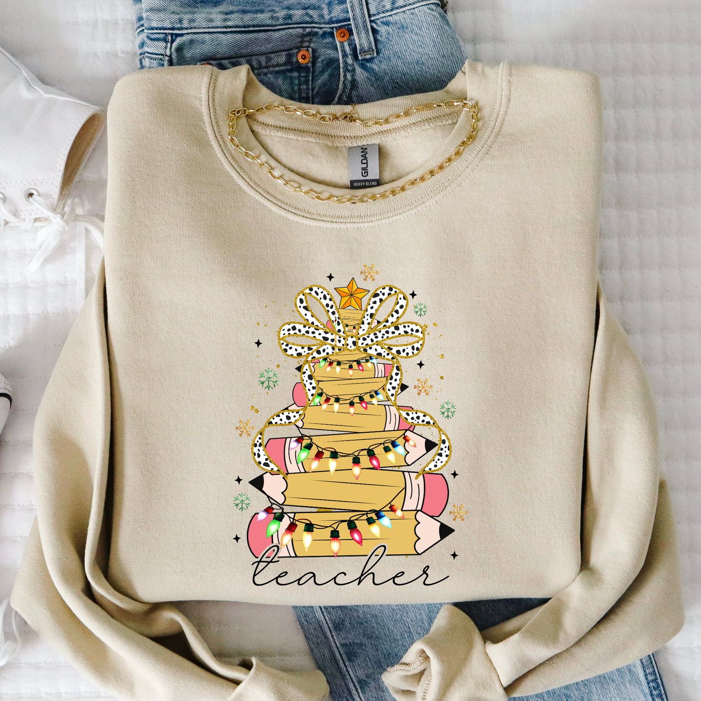 Beige sweatshirt with a 'teacher' design featuring books and lights, folded on a white surface.