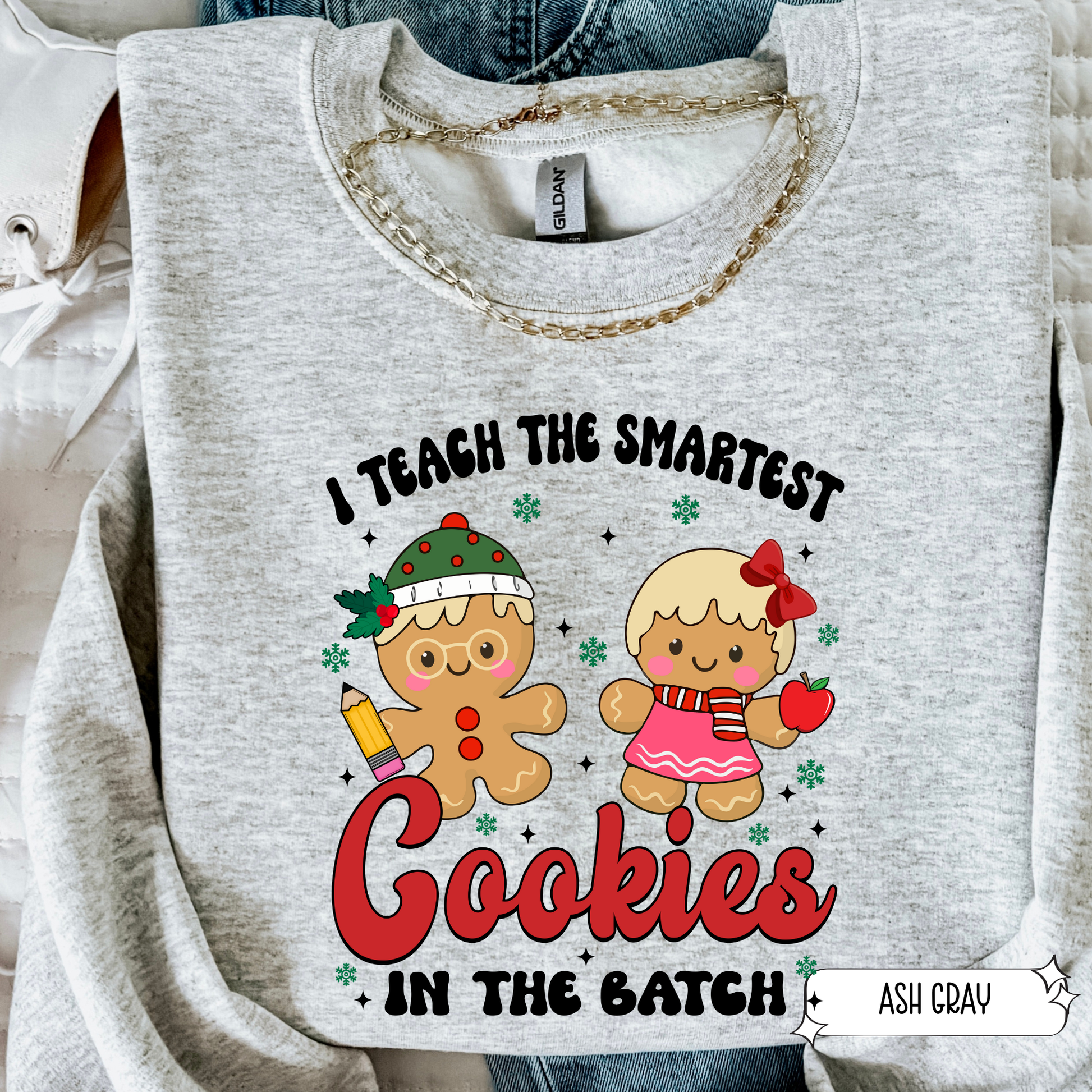 Ash gray teacher Christmas sweatshirt with gingerbread cookie design and ‘Smartest Cookies in the Batch’ text in flat lay.