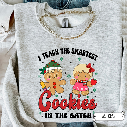 Ash gray teacher Christmas sweatshirt with gingerbread cookie design and ‘Smartest Cookies in the Batch’ text in flat lay.