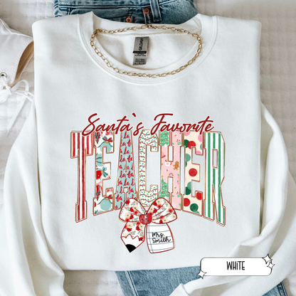 White Christmas teacher sweatshirt with Santa’s Favorite Teacher design featuring colorful stripes and bow, flat lay photo.