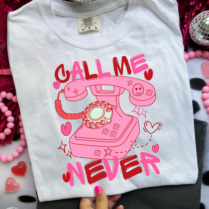 White t-shirt with pink telephone graphic and 'Call Me Never' text on a colorful background.