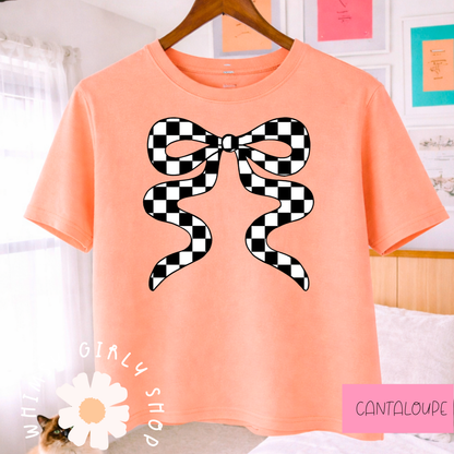 cantaloupe t-shirt with a black and white checkered bow design, hanging on a wooden hanger.