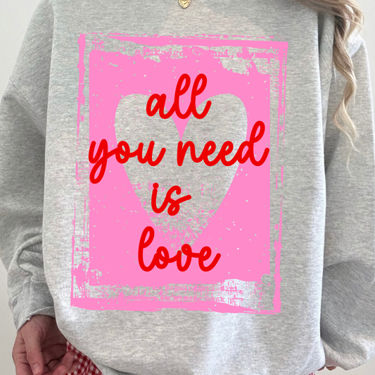 Gray sweatshirt with a pink heart and red text 'all you need is love' on a person wearing it.