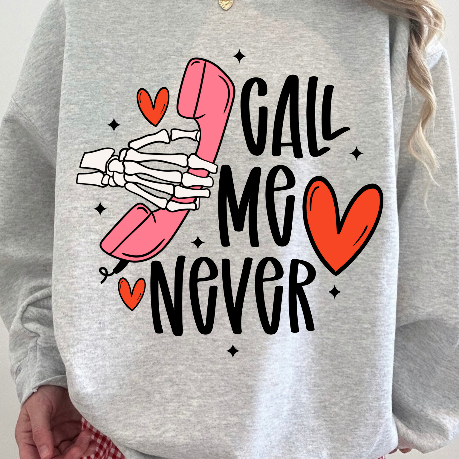 Gray sweatshirt with skeleton hand holding pink phone and 'Call Me Never' text on a plain background