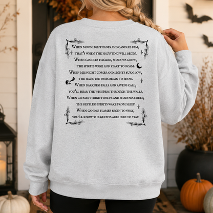 A person wearing a light gray sweatshirt with a black printed poem about haunted houses and candles, posed in a Halloween-themed setting with pumpkins and bats in the background.