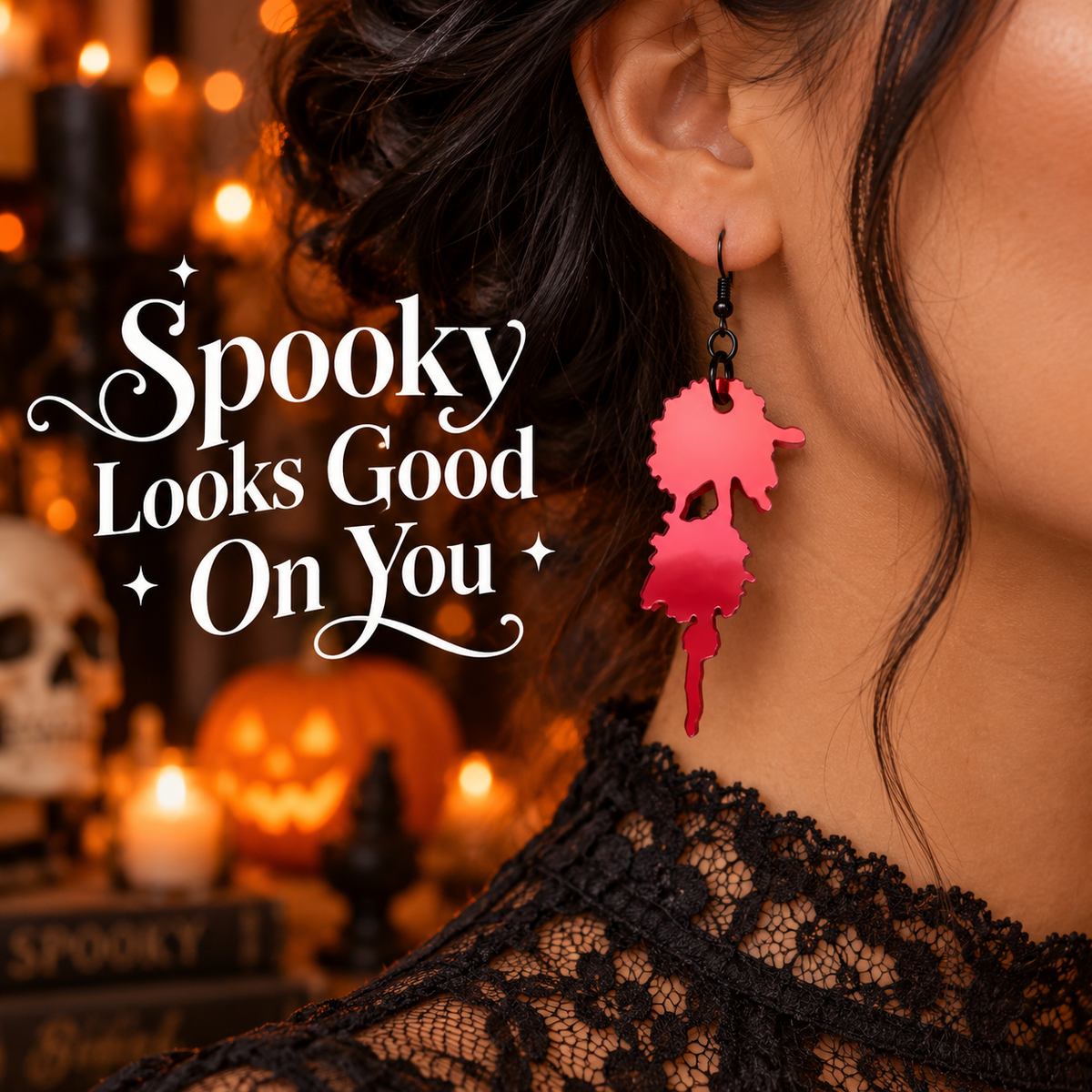 A close-up lifestyle shot of a woman wearing a dangling red  Halloween earring shaped like a dripping blood. The background is a warm, spooky Halloween scene with candles, a jack-o'-lantern, and the text 'Spooky Looks Good On You' overlaid on the left.
