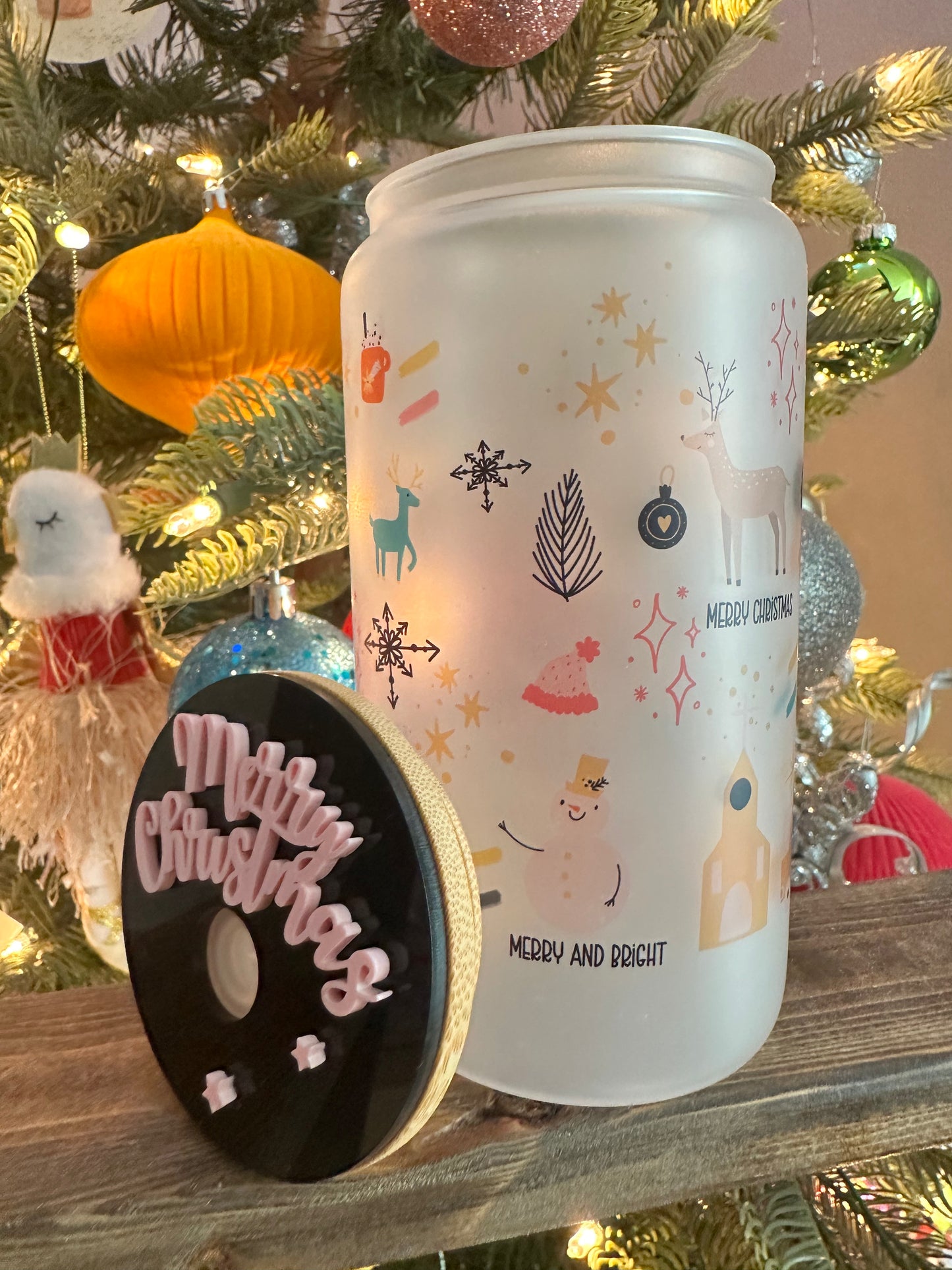 Decorative can with Christmas-themed illustrations on a wooden surface with a Christmas tree in the background.