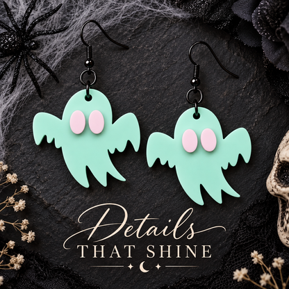 A pair of dangling ghost-shaped earrings in mint green with pale pink oval eyes and black fishhook wires, displayed on a dark textured surface with Halloween-themed props and the text 'Details That Shine'.