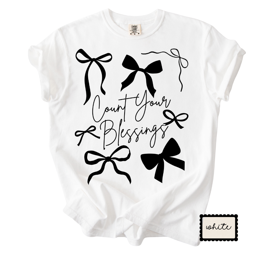 White t-shirt with black bows and 'Count Your Blessings' text on a white background