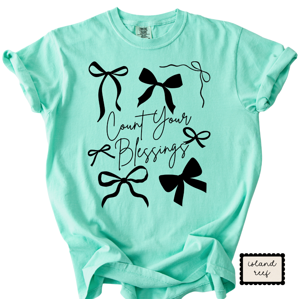 Mint green t-shirt with black bows and 'Count Your Blessings' text on a white background