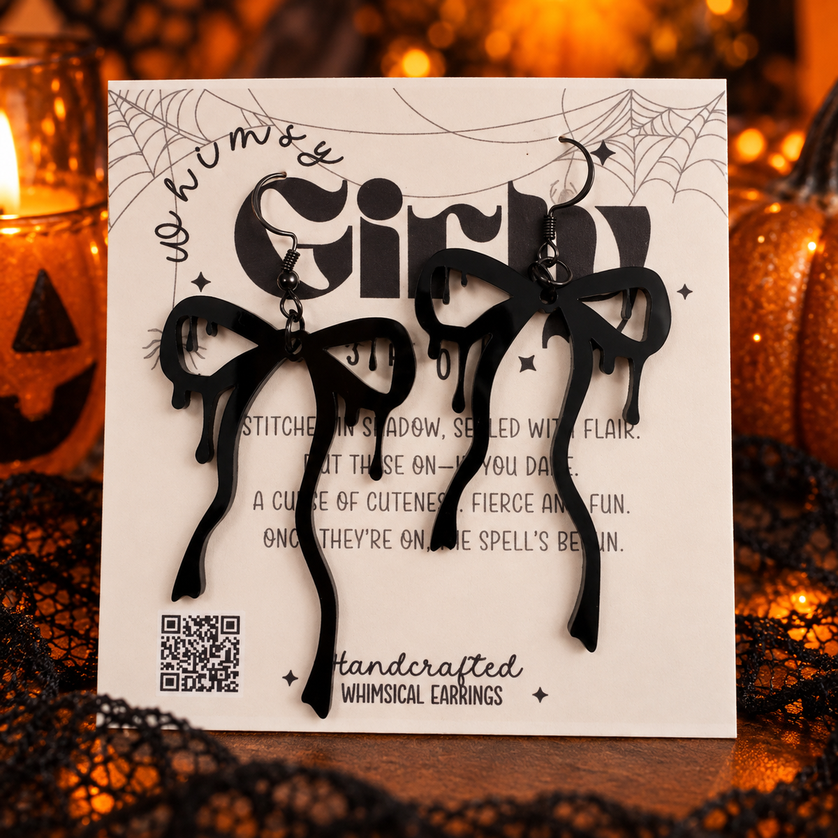 Black bow-shaped dangling earrings displayed on a white backing card with gothic text and spiderweb graphics, set against a warm Halloween-themed background with orange lights and black lace.