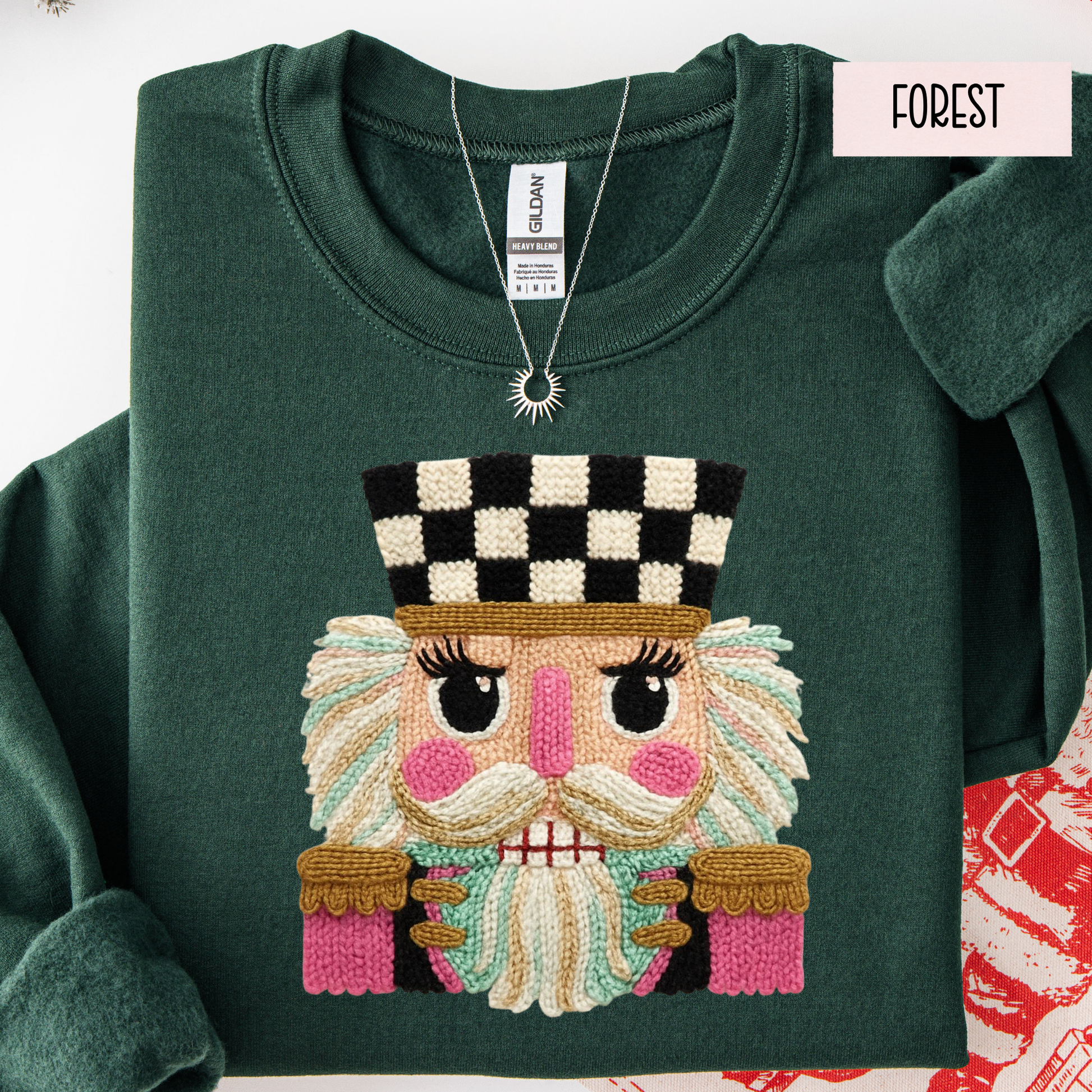 Folded green sweatshirt with faux yarn embroidered face design on a white background