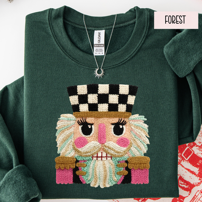 Folded green sweatshirt with faux yarn embroidered face design on a white background