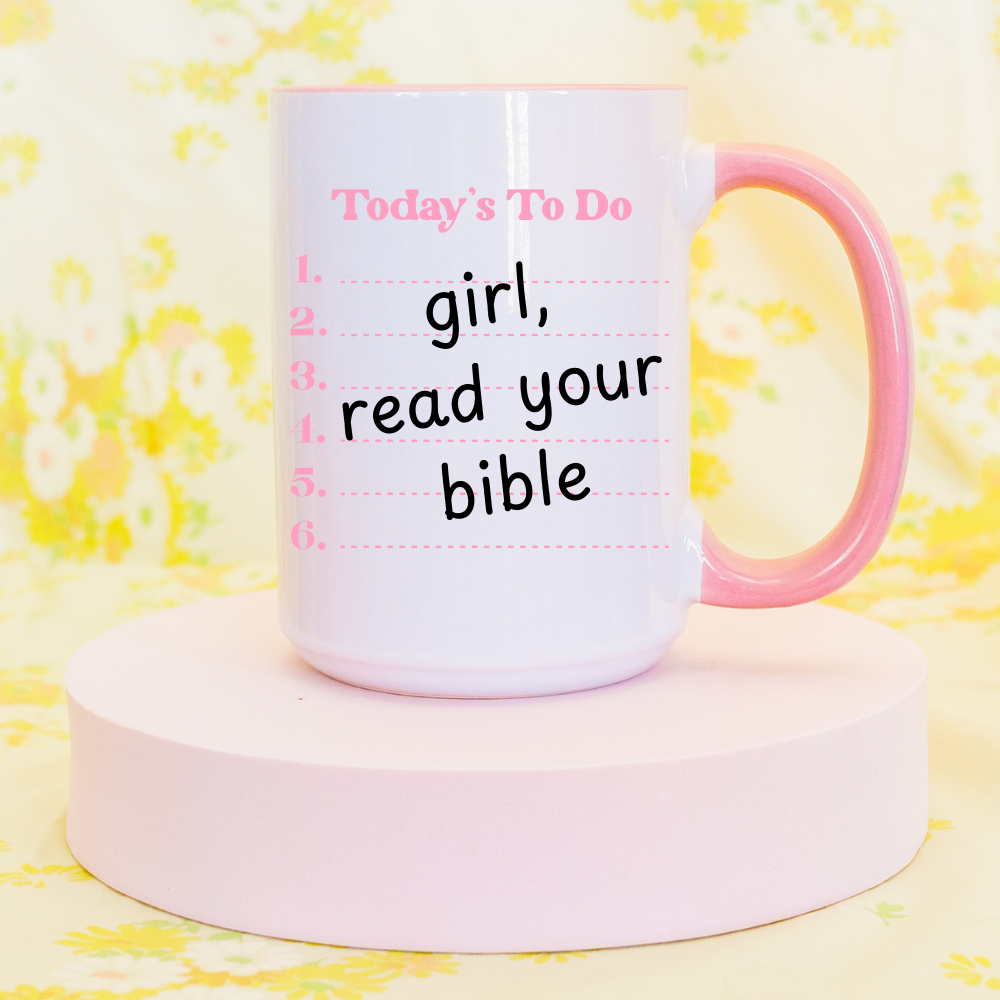 Pink 15oz Christian motivational mug with ‘girl, read your bible’ design displayed on a pastel stand.