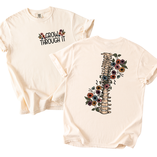 Cream Comfort Colors T-shirt with “Grow Through It” floral graphic on the front and a detailed floral spine illustration on the back.

If you want, I can also c