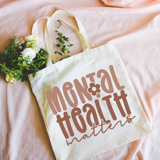 Tote bag with 'Mental Health Matters' text on a pink surface with flowers.