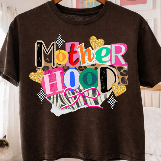Brown t-shirt with colorful 'Motherhood' graphic design in a bedroom