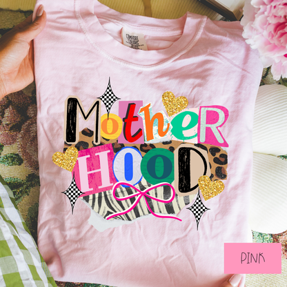 Pink t-shirt with colorful 'Mother Hood' text and decorative elements, held by a hand.